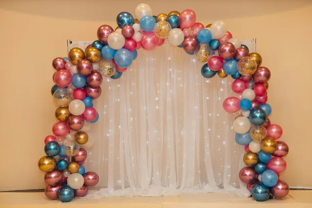 Arco de globos metalizados rosas, azules y dorados delante de una cortina de luces