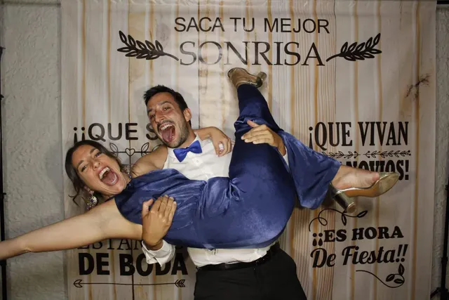 Pareja de invitados posando en el fotomatón de una boda, delante del fondo «Saca tu mejor sonrisa»
