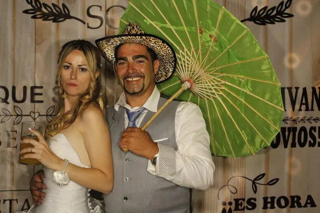 Novios con sombrero y sombrilla del atrezzo posando en el fotomatón el día de su boda